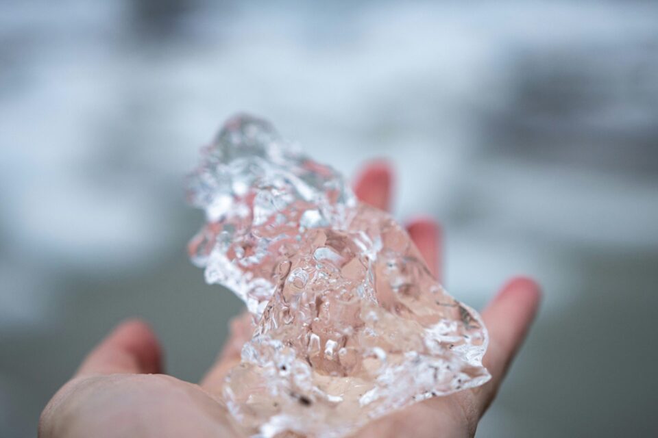 a hand holding a large chunk of clear ice