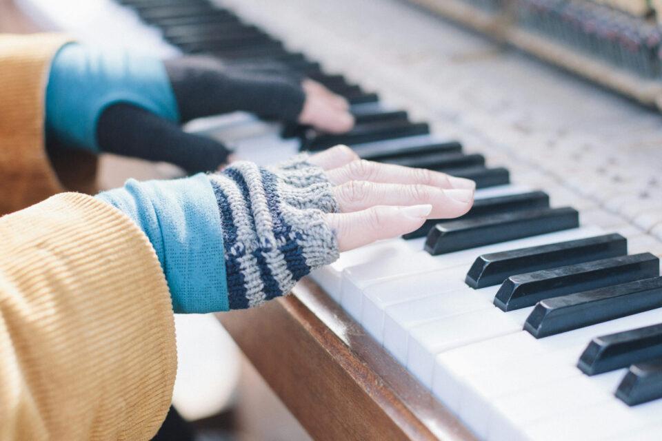close up of someone's hands playing the piano. They are wearing stripy fingerless gloves