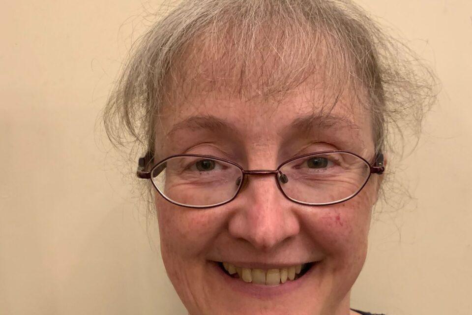 A woman in glasses and a grey top smiling