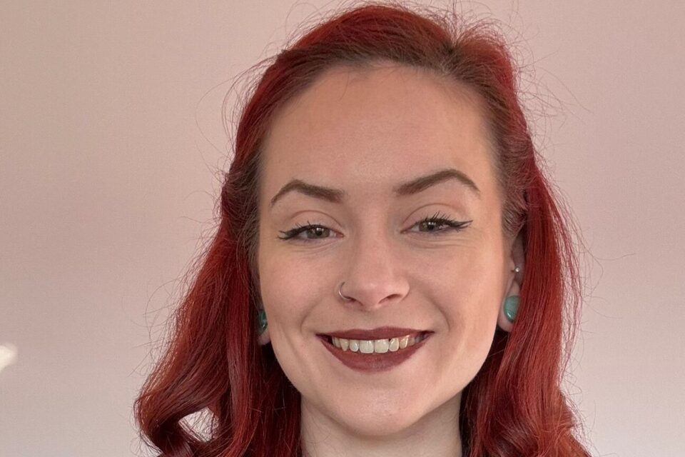 A young woman with red hair and wearing a black cardigan