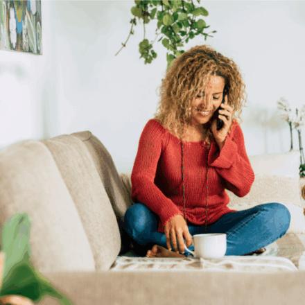 a woman sitting on her sofa with a cup of tea, talking on the phone