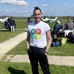 A man wearing an SRUK t-shirt, at an airfield